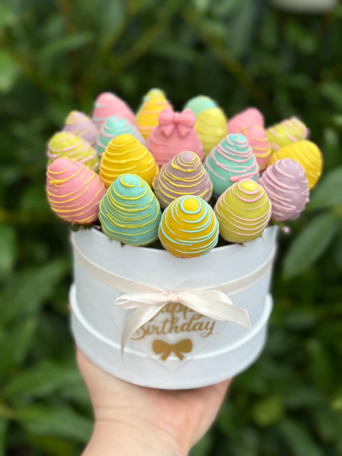 Cheerful pastel-coloured chocolate strawberries in a white birthday hatbox